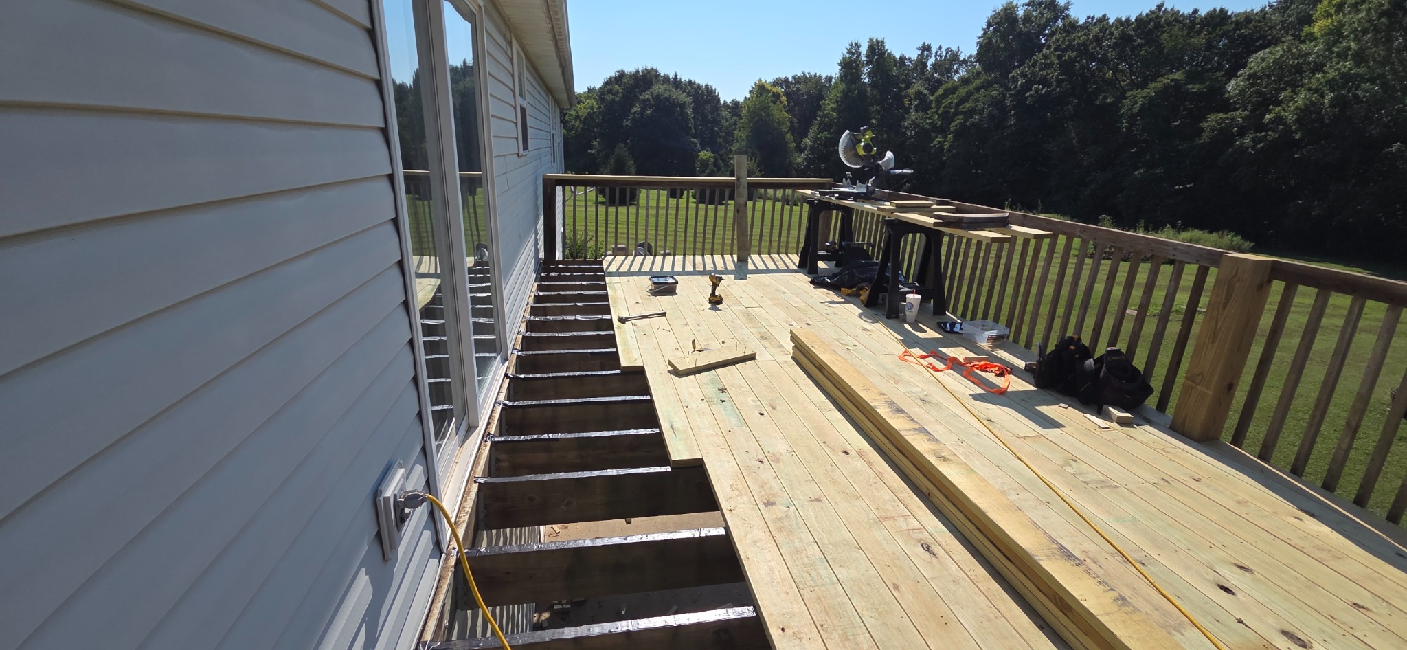 Deck board replacement in progress with exposed joists beside new decking